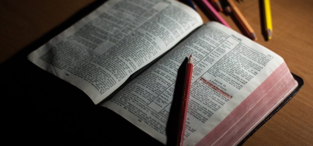 An open Bible on a wooden table accompanied by colored pencils, symbolizing study and spirituality.