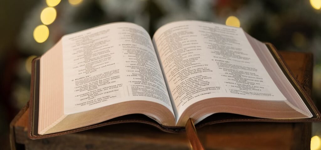 Open Bible resting on wooden surface with blurred festive background lights.