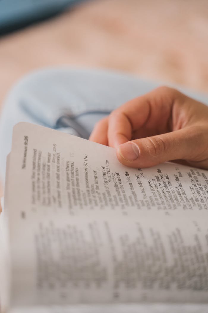 A close-up photo capturing a hand holding open a Bible, focusing on text.