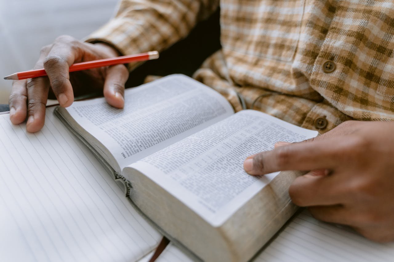 Hands holding an open Bible while taking notes with a pencil.