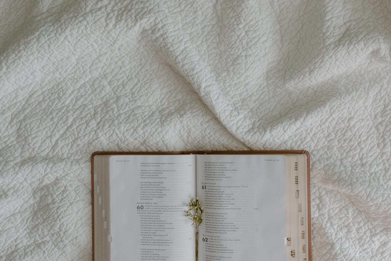 An open Bible on a white quilted fabric background with a small flower arrangement.
