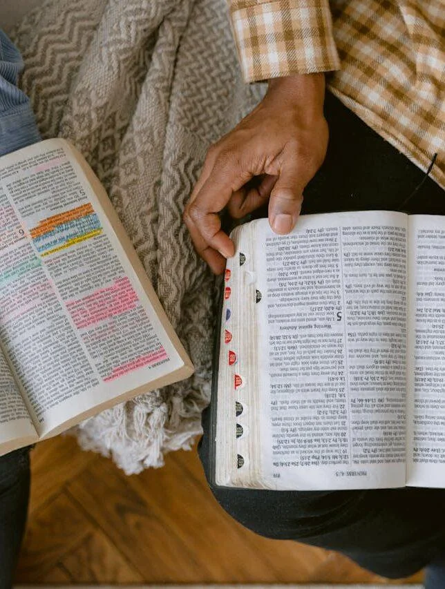 Two adults reading religious texts with highlighted passages indoors, sharing a moment of learning and connection.